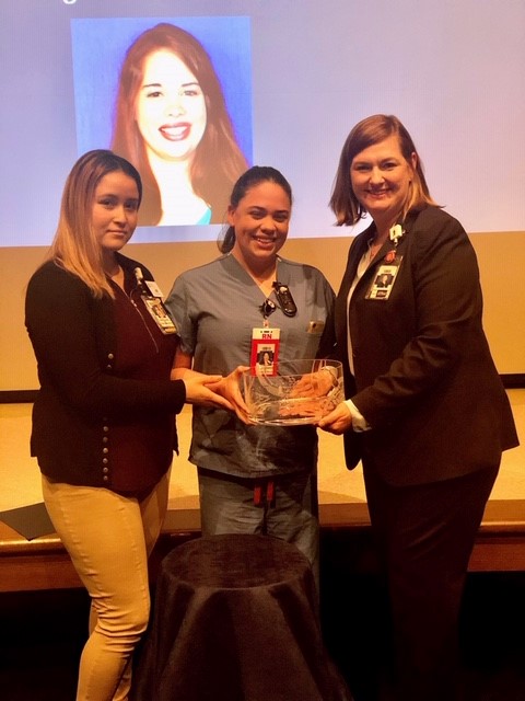 three women hold award in front of projected image on white screen.