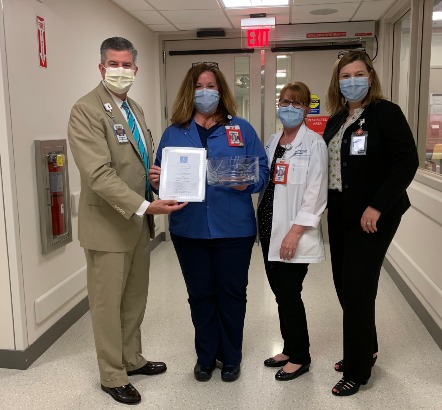 four people standing in hospital hallway, wearing masks and holding award.