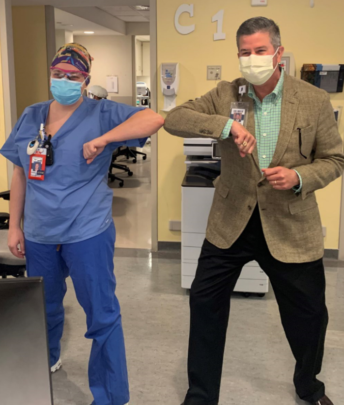 man in suit and medical worker masked and bumping elbows to pose for camera.